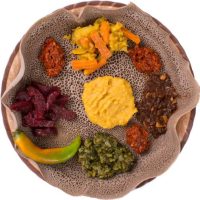 Top view of Ethiopian injera - a spongy sourdough flatbread made of fermented teff flour, spread flat over a communal pan (a large platter) and topped with several kinds of wats (stews) and vegetables. Injera bread isolated over white background.